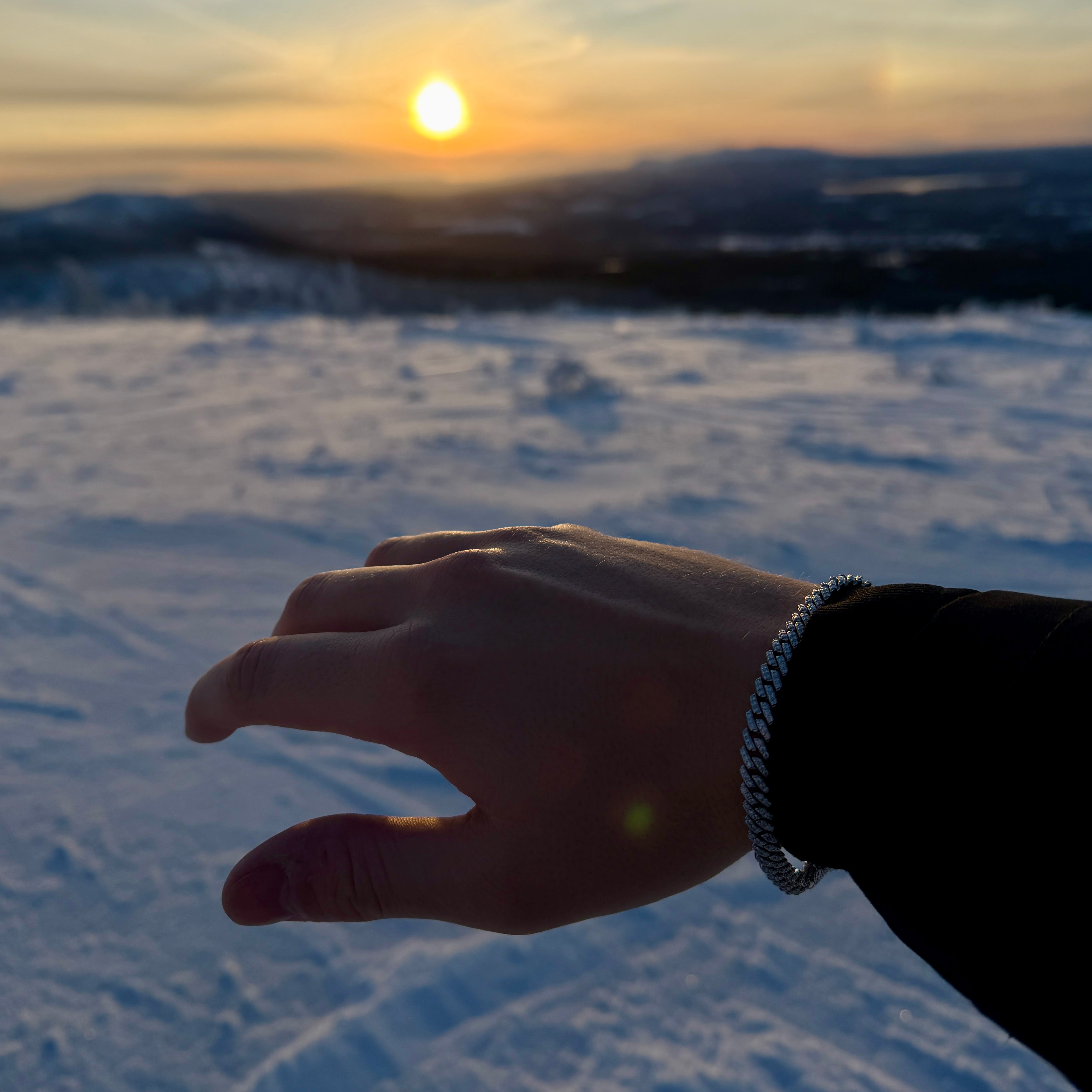 Hand wearing ROYAL ICE VVS1 18K White Gold Cuban bracelet against a sunset backdrop over snowy mountains.