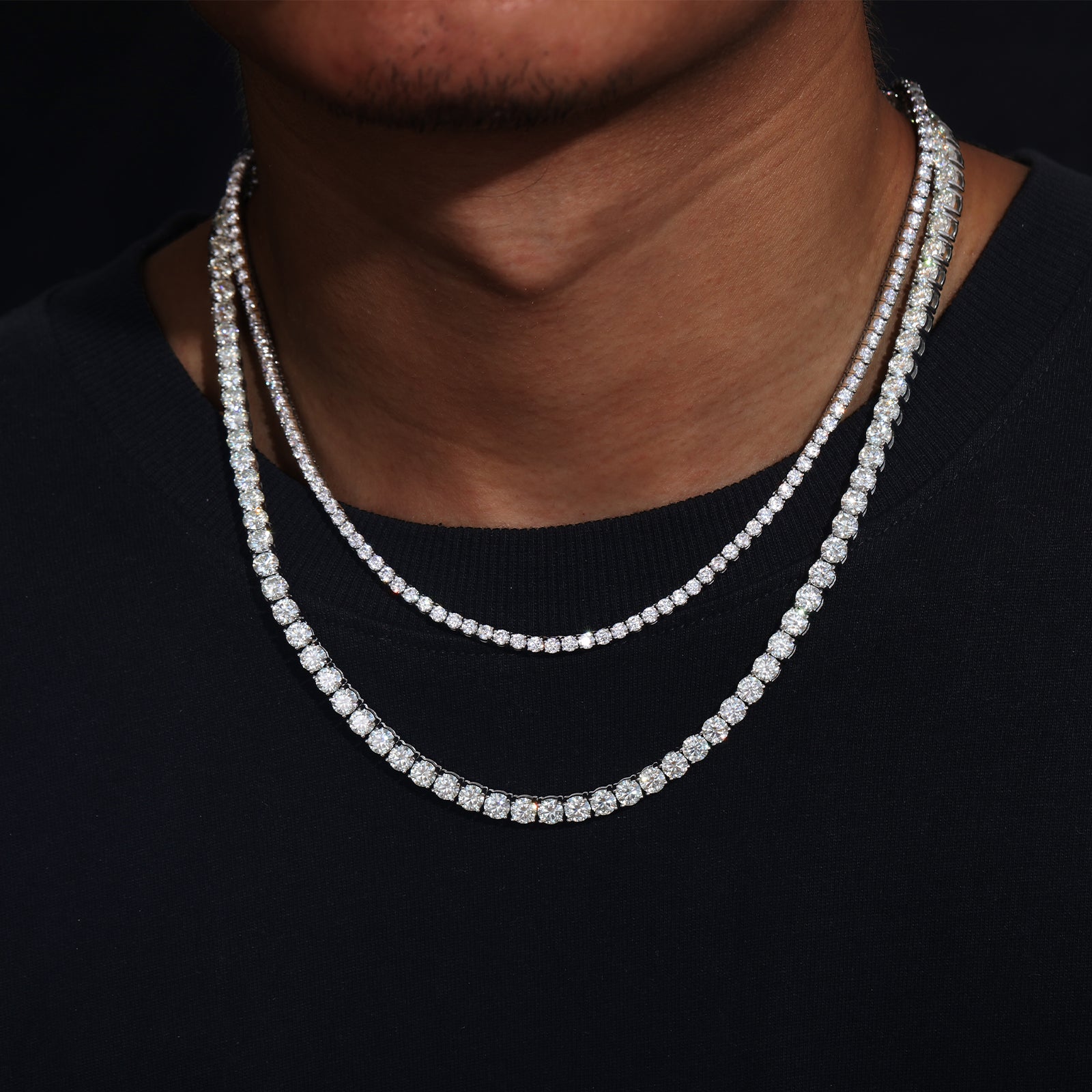 Close-up of a person wearing two diamond necklaces on a black background